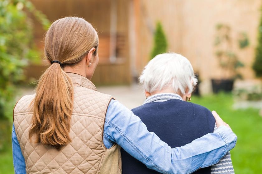 Frau begleitet eine Seniorin bei einem Spaziergang im Garten